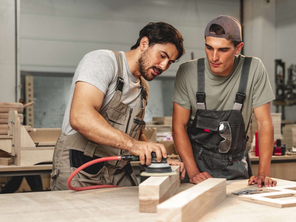 Two,Young,Carpenters,Working,With,Wood,Standing,At,Table,In