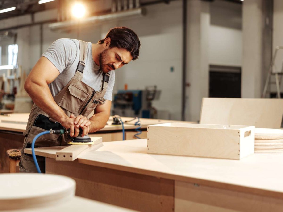 Young,Carpenter,Sanding,Wood,Piece,In,Workshop,In,Furniture,Factory